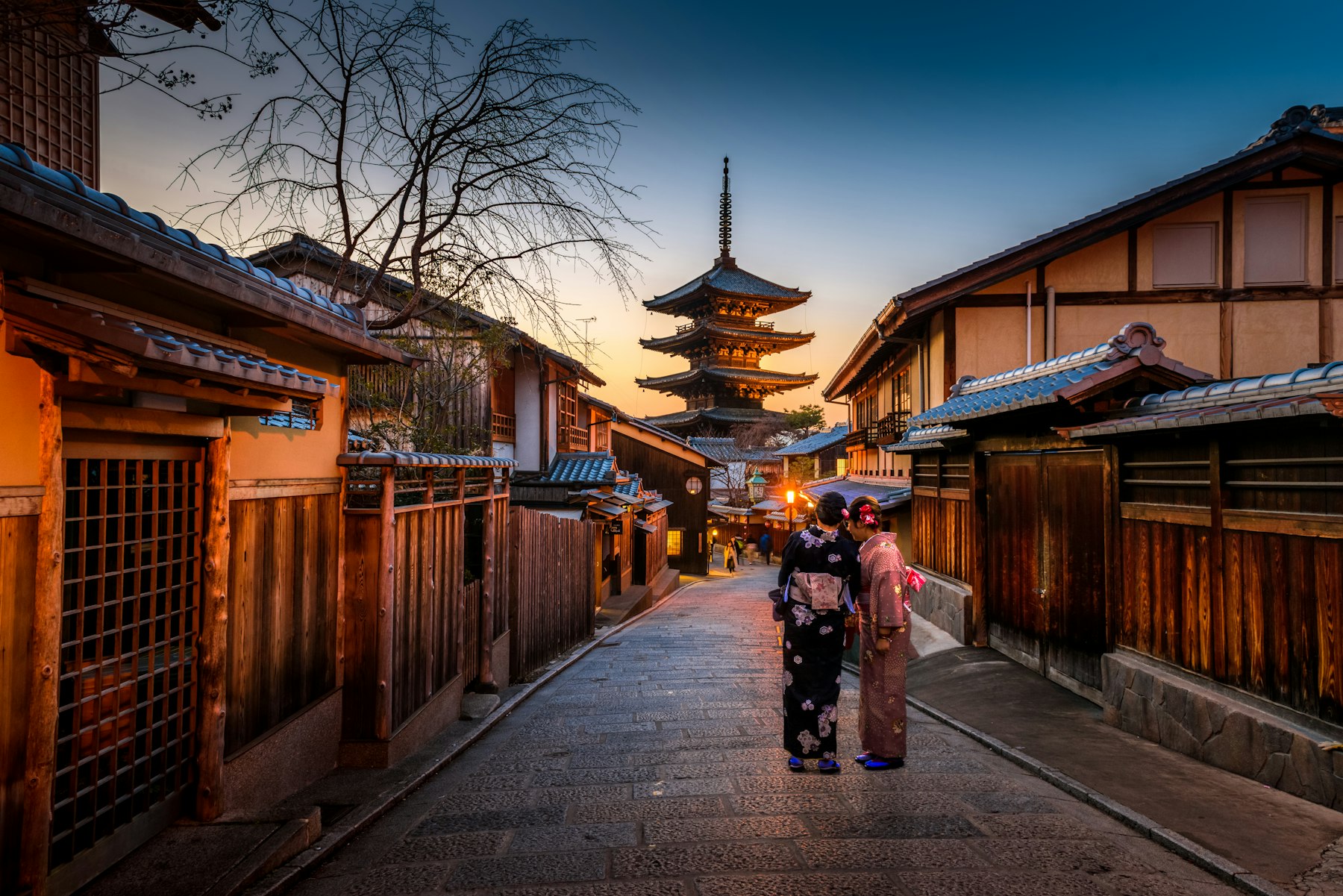 A pagoda at dusk above a Kyoto street, with two women in kimono
