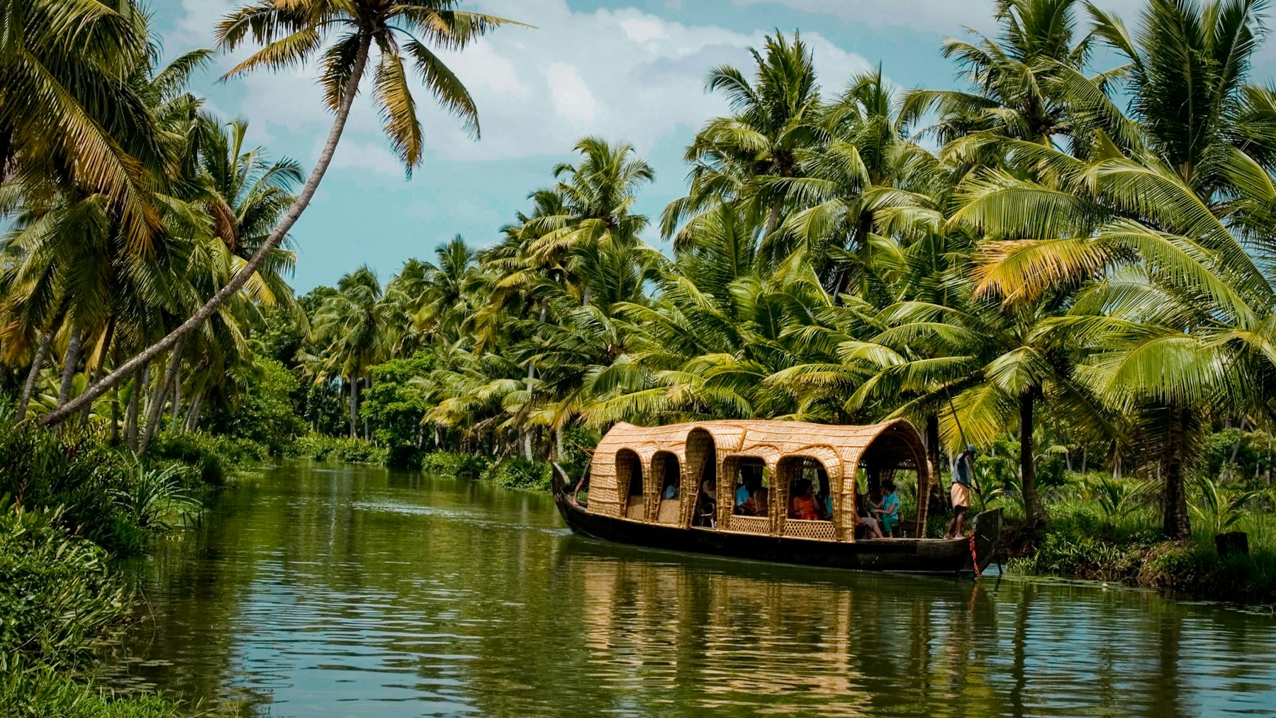 Houseboat moving through a narrow palm canal in Kerala