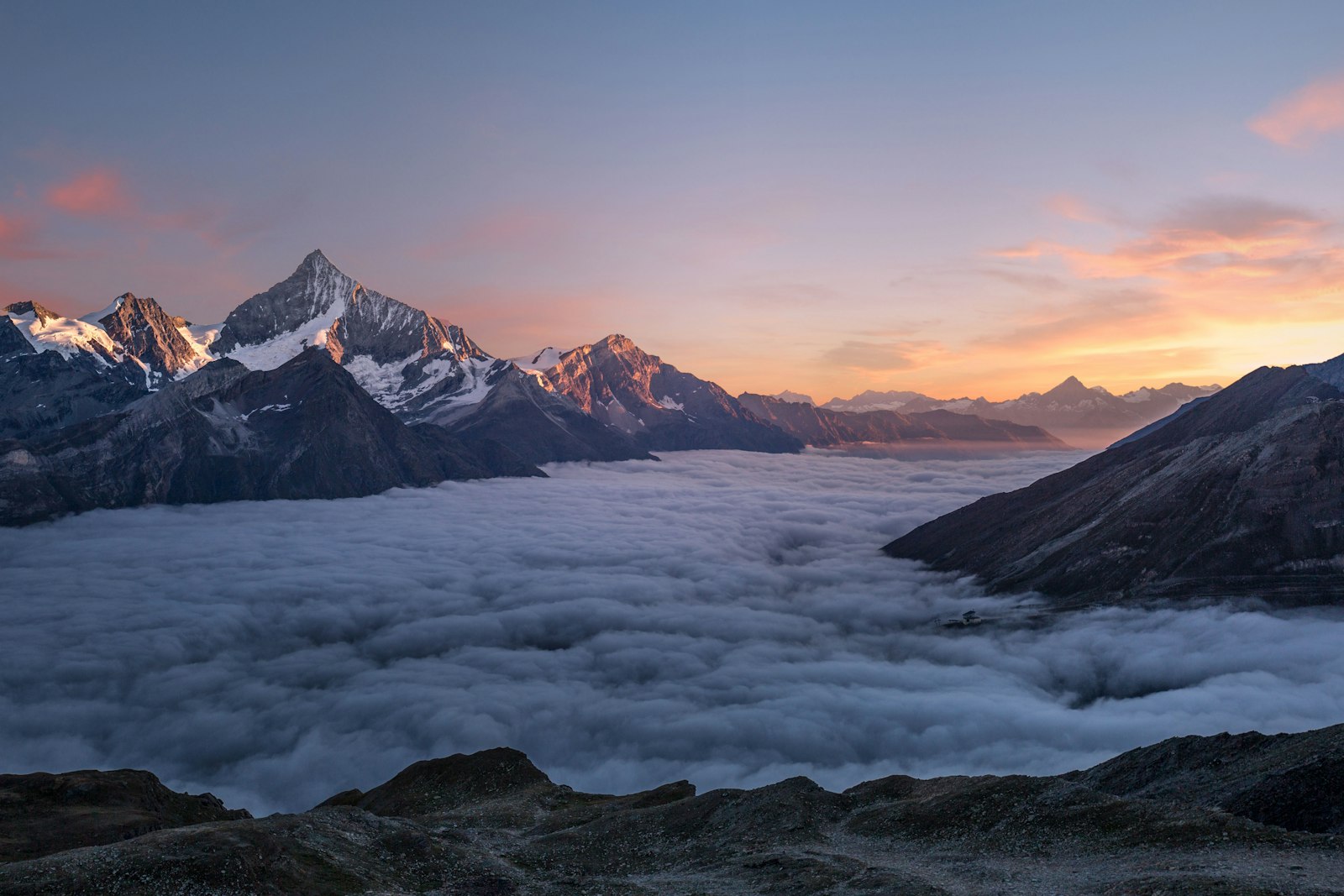 Snow peaks rising above a sea of clouds at sunrise